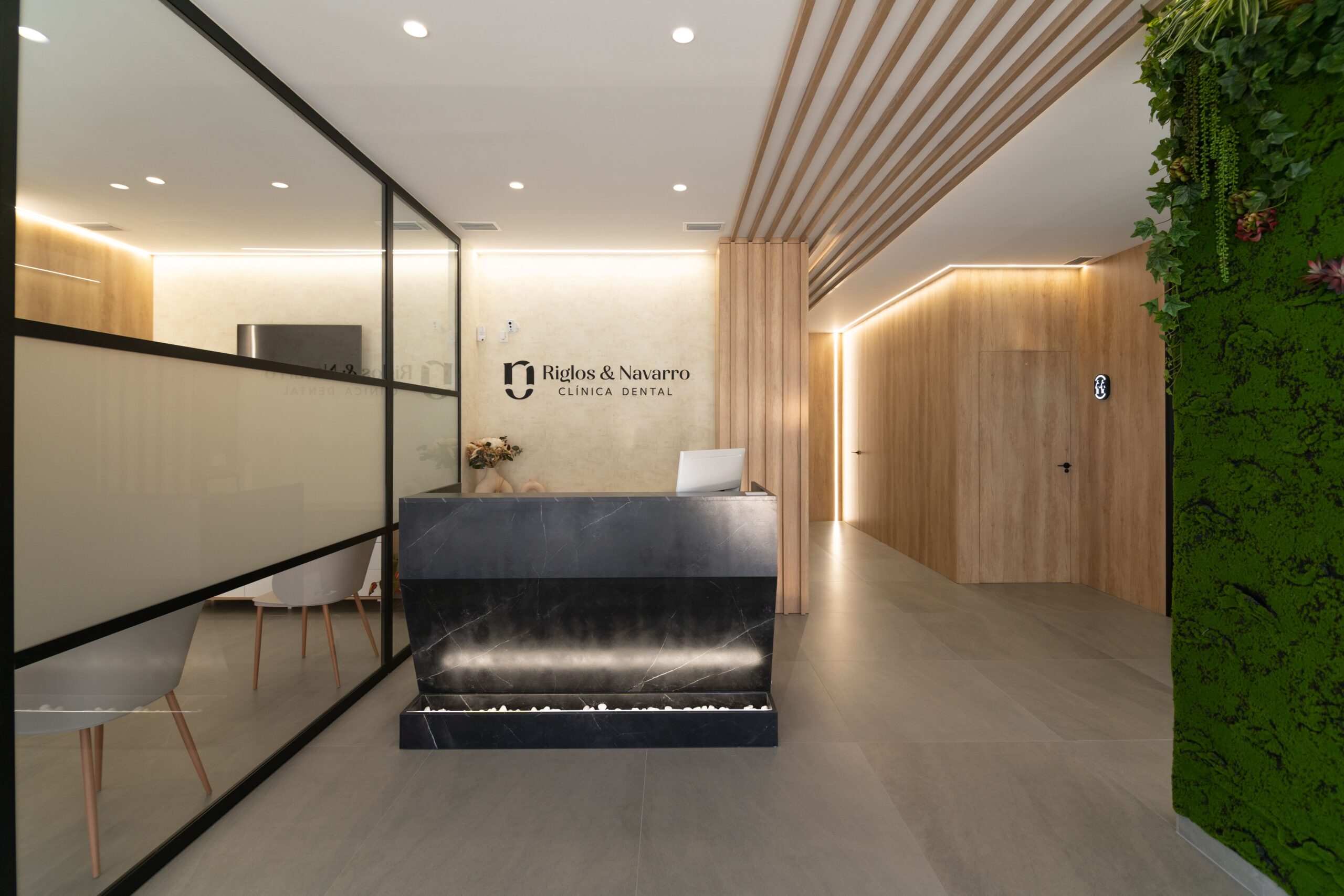 Mostrador de la clinica dental a la izquierda esta la sala de espera separada con una cristalera y a la derecha el pasillo con los boxes